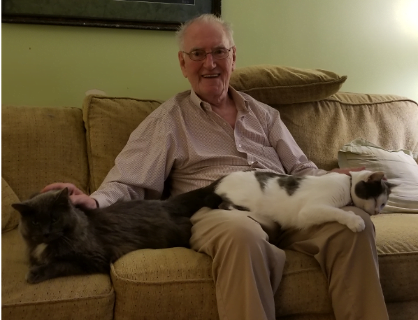 Elderly man sitting on a couch with white and black cats